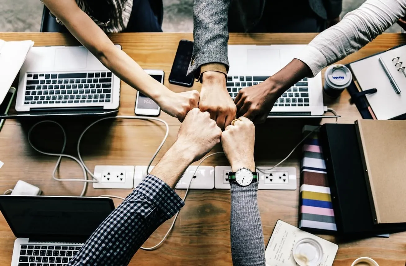 A team joining hands over laptops